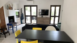 A modern living room with a black dining table, yellow and white chairs, a black sofa, and a TV mounted on the wall. - Villa del Brigante, 200m to the beach, 80m² (Quartu Sant'Elena)