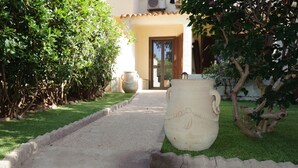 A pathway leading to a building with a door, surrounded by greenery and large vases. - Villa del Brigante, 200m to the beach, 80m² (Quartu Sant'Elena)