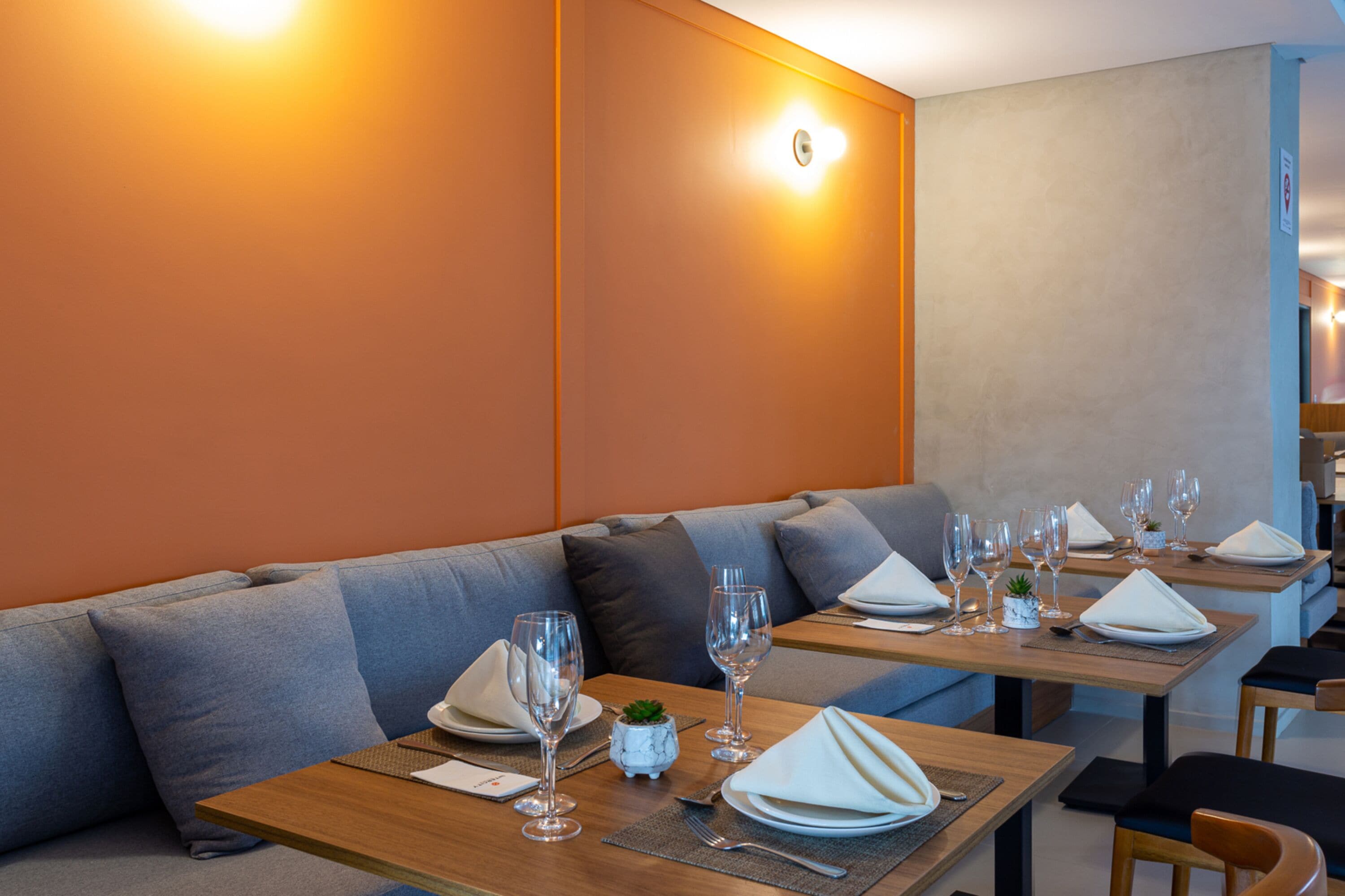 Un espace repas moderne avec des tables en bois, des sièges rembourrés de couleur grise et une vaisselle disposée avec soin.