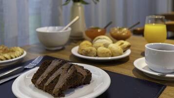A breakfast table with a slice of chocolate cake, a bowl of fruit, a cup of coffee, and a glass of orange juice.