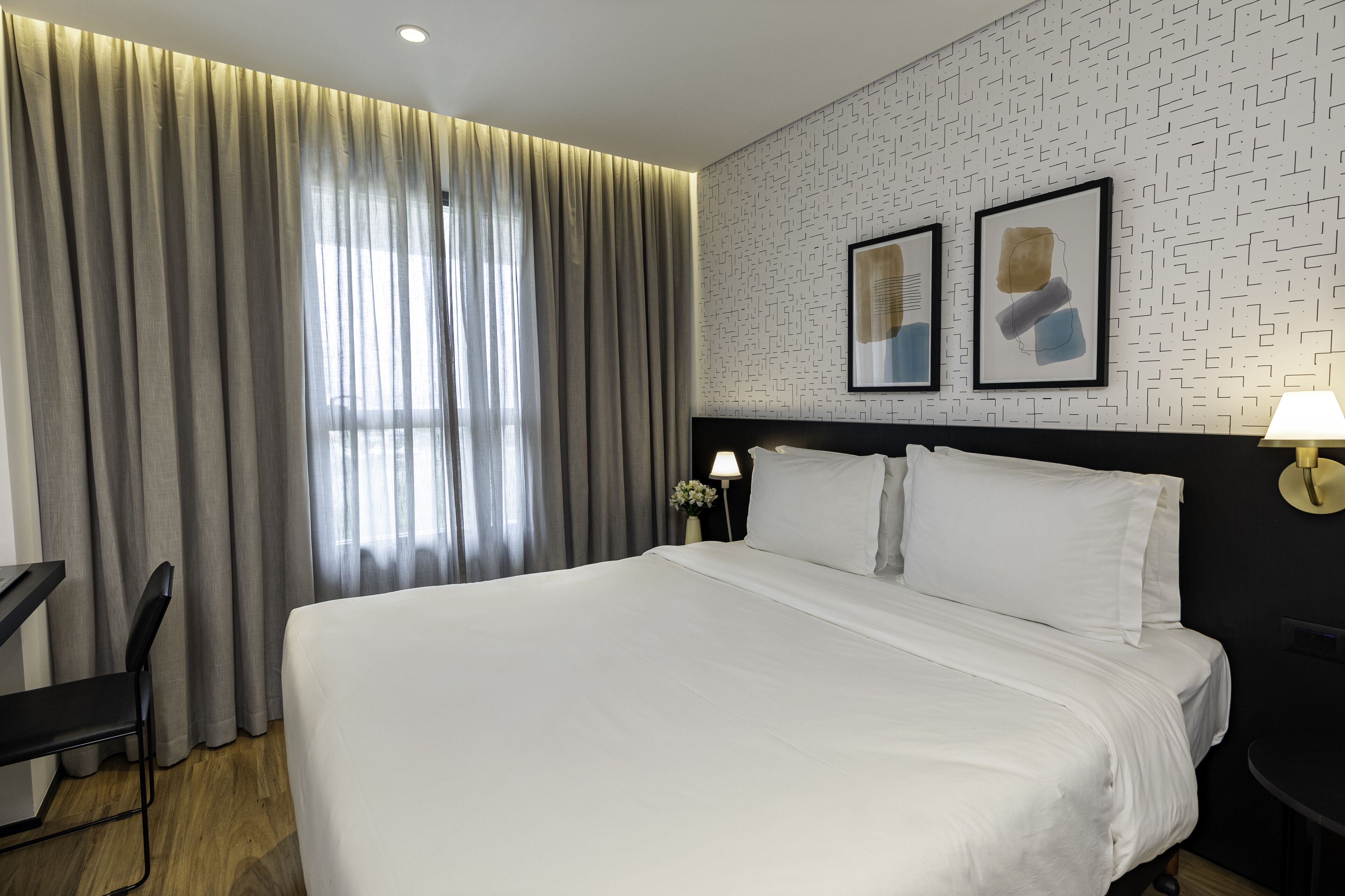 Ett hotellrum med en stor säng, ett skrivbord, en stol och ett fönster med gardiner.