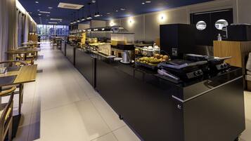 A modern hotel kitchen with a buffet, dining tables, and a view of the city.