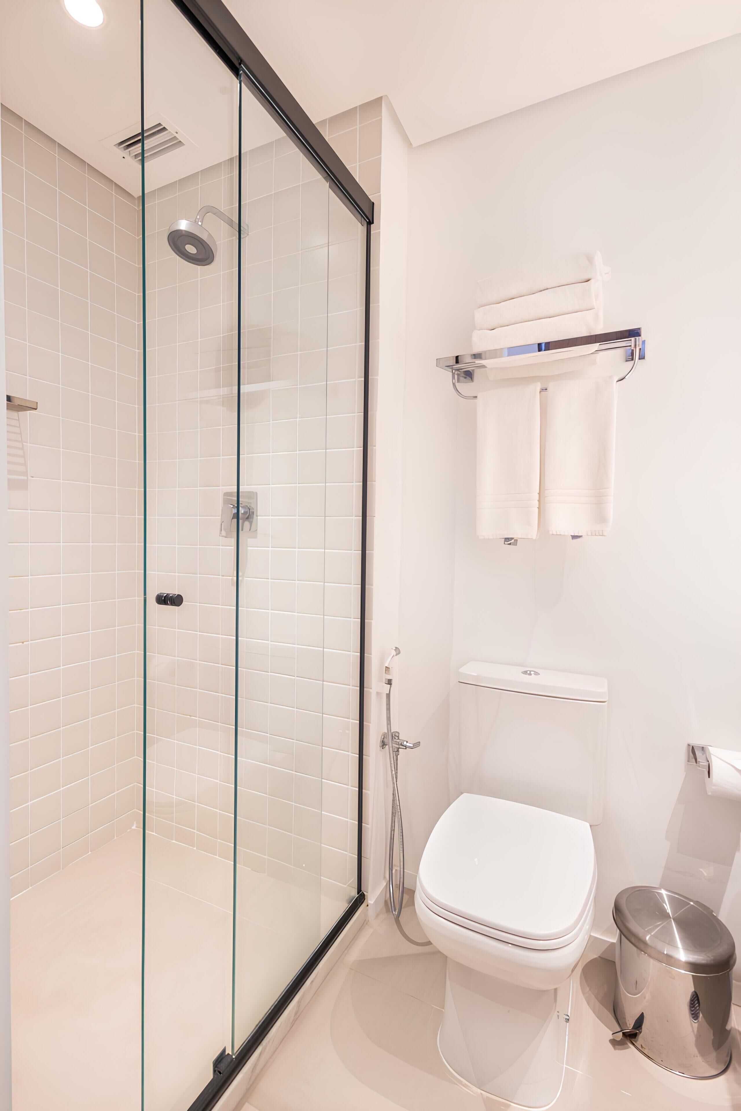 Une salle de bain moderne avec une douche à parois de verre, des toilettes blanches et une poubelle.