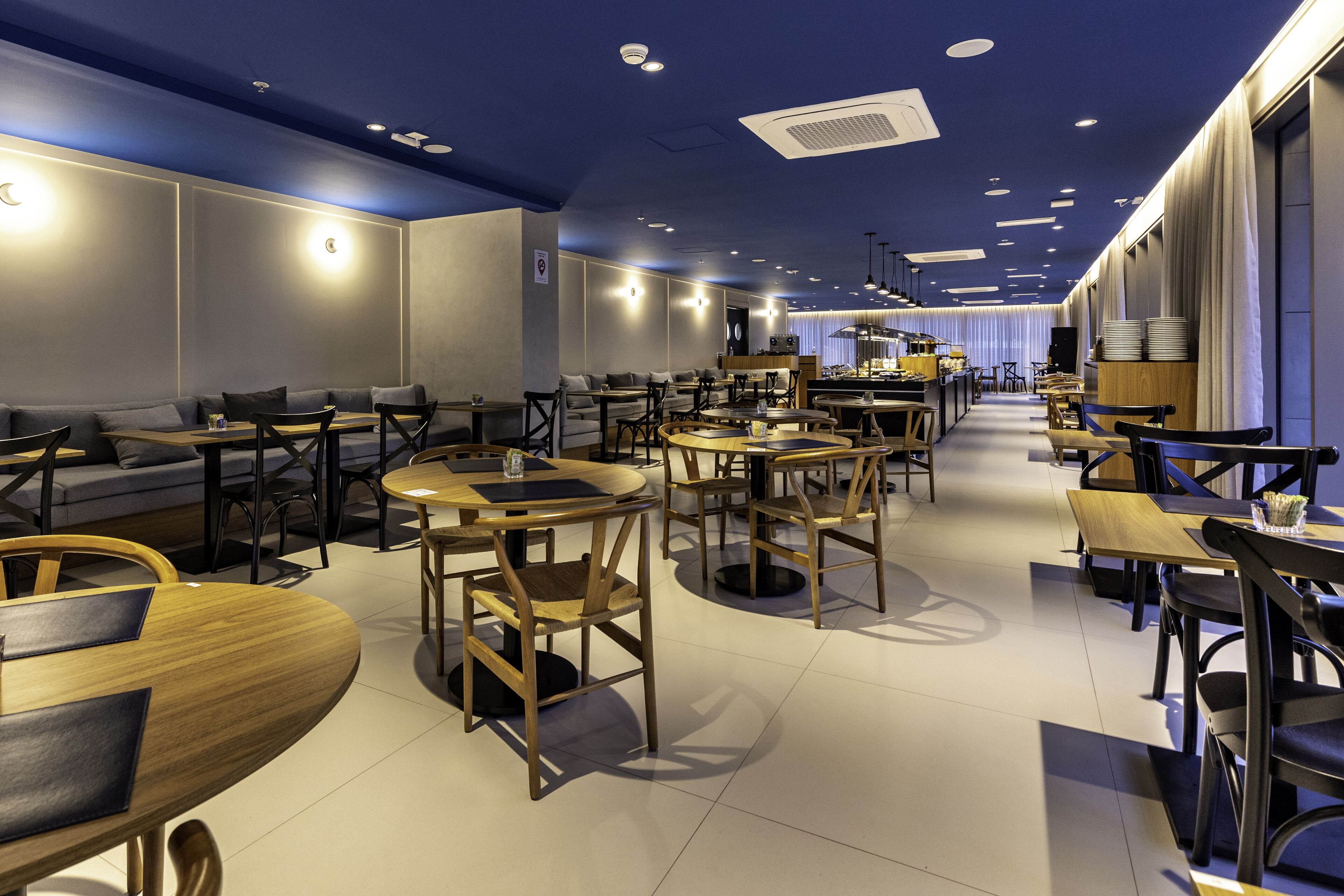 A modern restaurant with round tables and chairs, a bar area, and a seating section with sofas and tables.