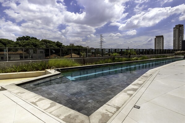 Una piscina con borde de baldosas, rodeada por una valla baja y follaje.