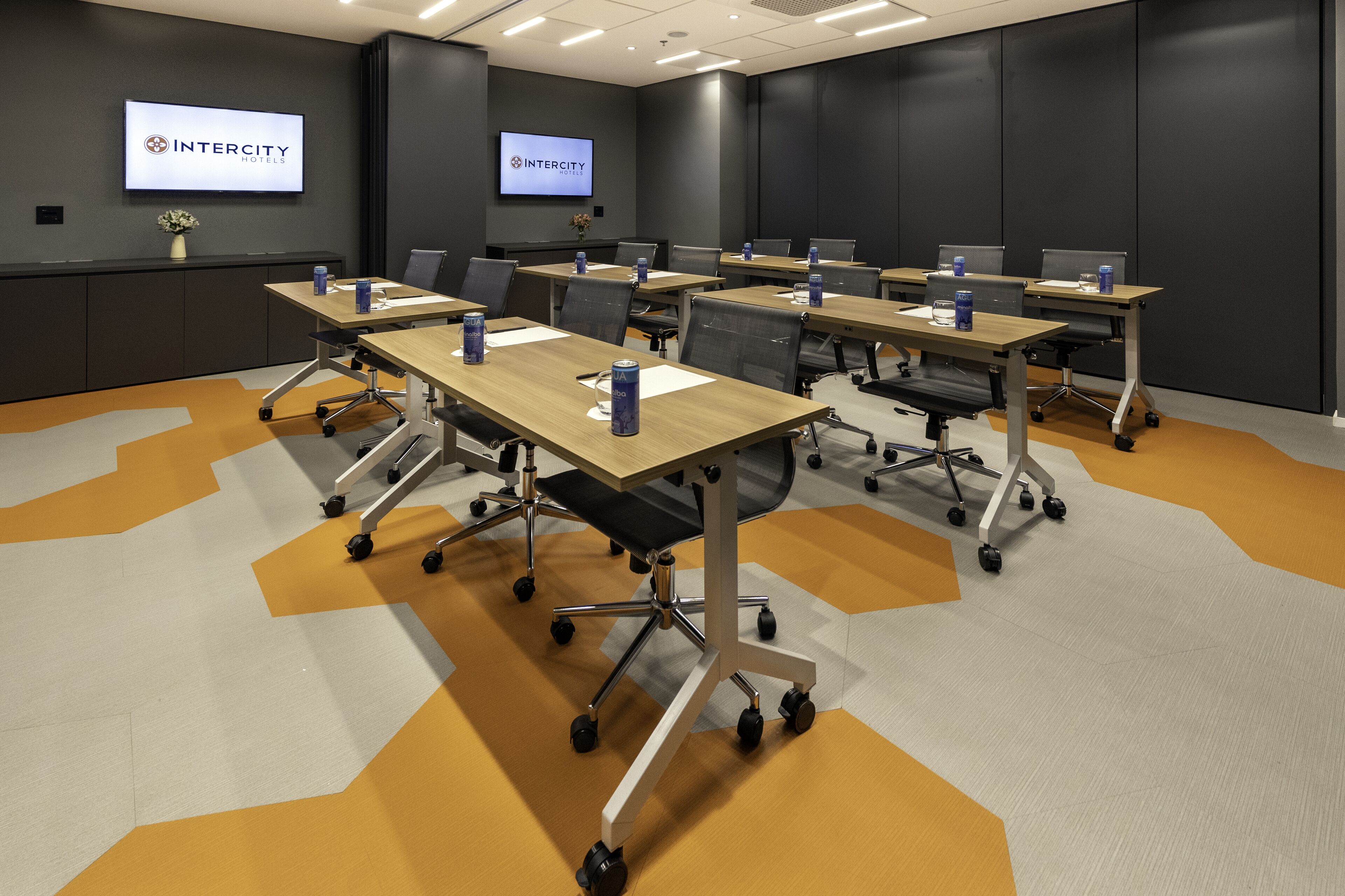 A conference room with multiple tables, chairs, and a large screen displaying the Intercity Hotels logo.