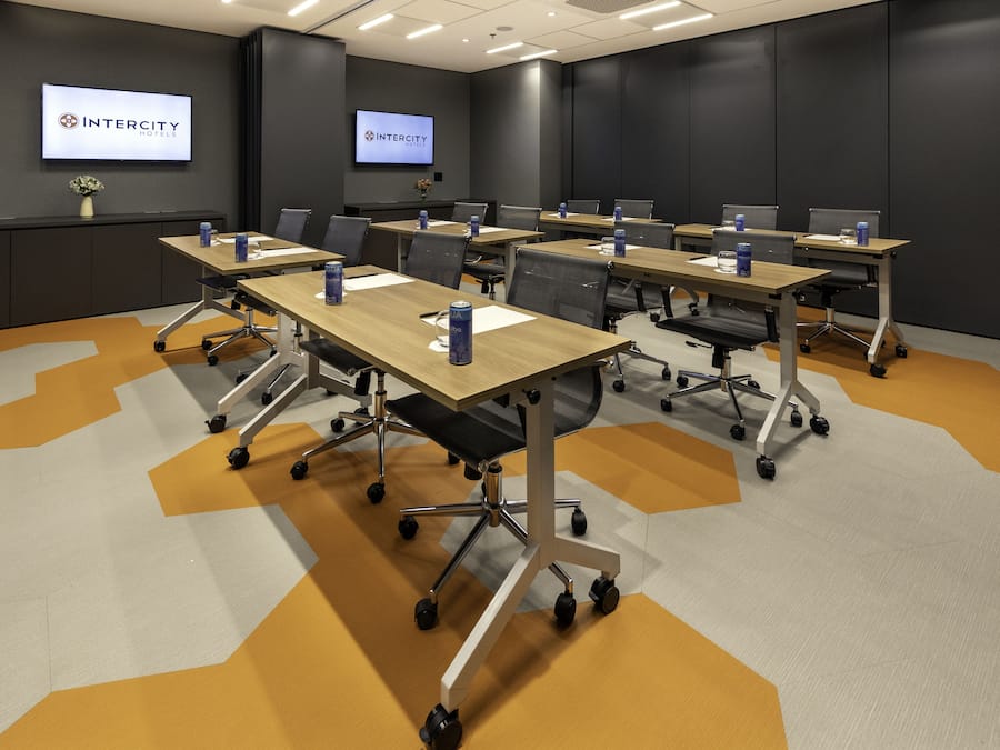 A conference room with multiple tables, chairs, and a large screen displaying the Intercity Hotels logo.