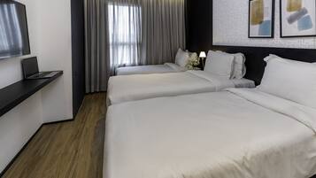 A hotel room with two beds, a desk with a laptop, a large window with curtains, and artwork on the wall.