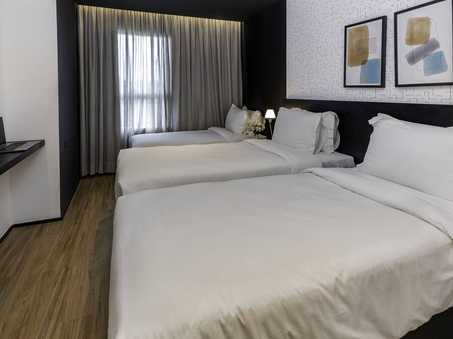 A hotel room with two beds, a desk with a laptop, a large window with curtains, and artwork on the wall.
