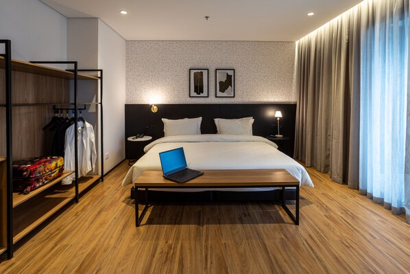 A modern hotel room with a wooden floor, a bed with a laptop, a wardrobe, and a nightstand with a lamp. - Intercity Tatuapé (São Paulo)