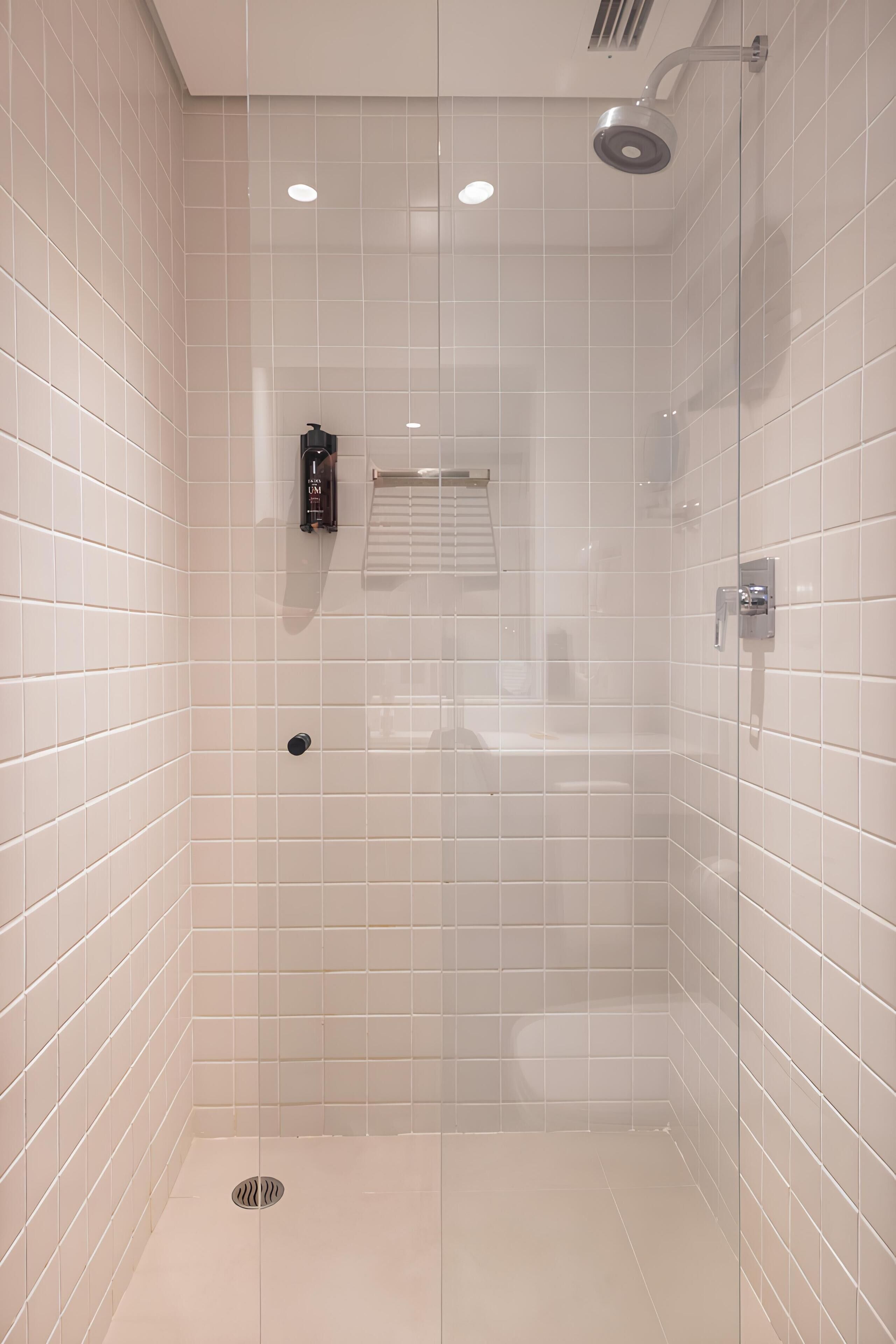 Eine moderne Dusche mit Glastür, weißen Fliesen und einer Handbrause.