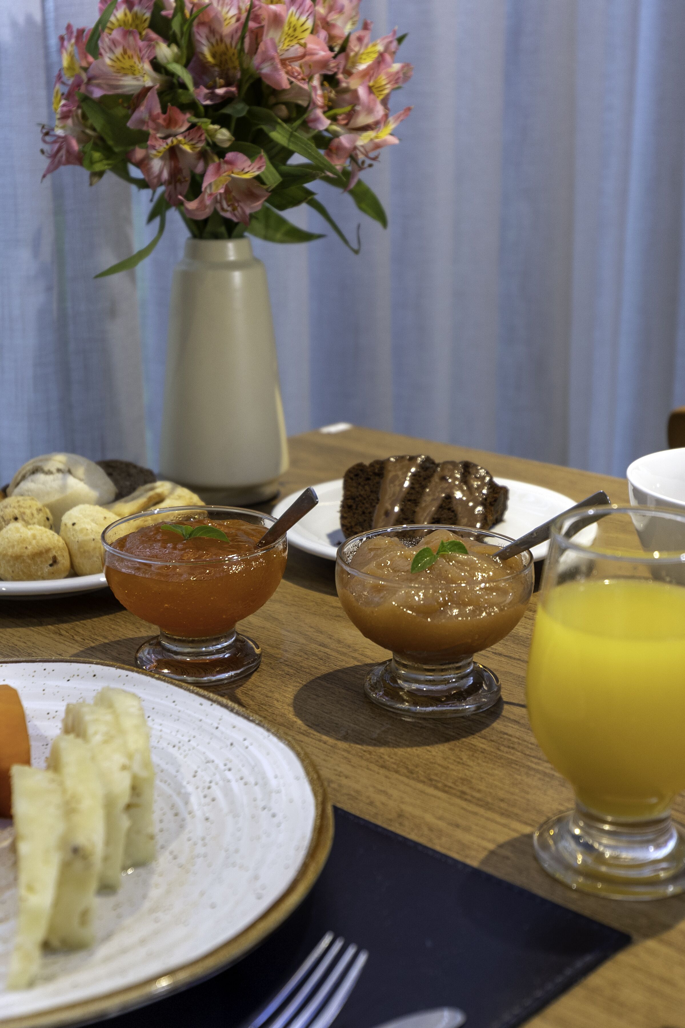 Uma mesa com diversos alimentos, incluindo um prato de doces, uma tigela de sopa e um copo de sumo de laranja.