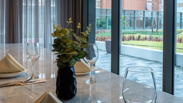 A dining area with a marble table, neatly set with plates, glasses, and cutlery. There are hanging pendant lights above the table, and a vase with green foliage on the table. - Intercity Tatuapé (São Paulo)
