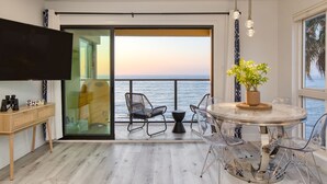 A modern living room with a large TV, a round dining table, and a balcony with a view of the sea. - Oceanfront in La Jolla, Steps to Beach, Shops, Dining | Dawn Patrol by AvantStay (La Jolla)