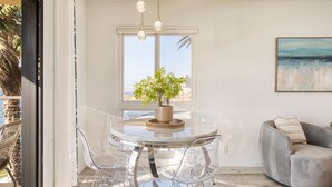 A modern living room with a glass dining table, clear chairs, a grey sofa, and a view of the ocean through a large window. - Oceanfront in La Jolla, Steps to Beach, Shops, Dining | Dawn Patrol by AvantStay (La Jolla)