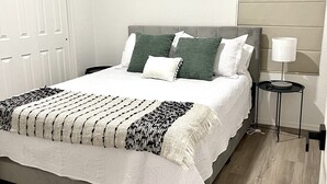 Una cama bien hecha con una colcha y almohadas de diseño blanco y negro, una mesita de noche con una lámpara y un suelo de madera.