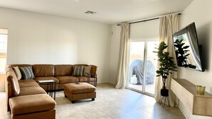 Una sala de estar con un sofá de cuero marrón, una mesita y un televisor montado en la pared.
