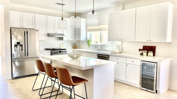Una cocina moderna con armarios blancos, un refrigerador de acero inoxidable, una estufa a gas y una isla grande con taburetes de bar.