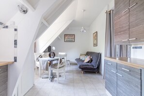 A modern kitchen with a dining area, a grey sofa, and a staircase.