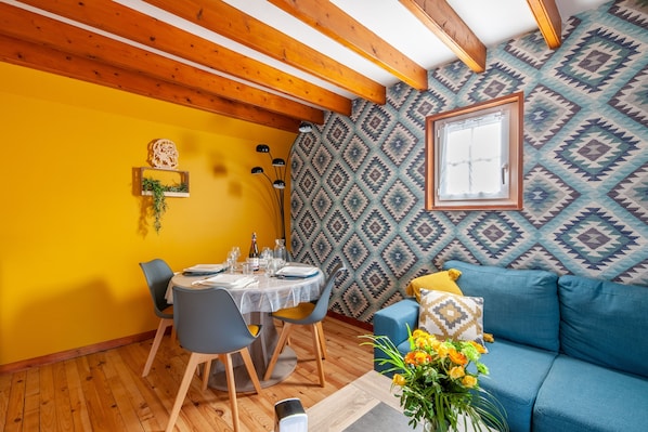A dining area with a wooden ceiling, a patterned wall, and a blue sofa with cushions.