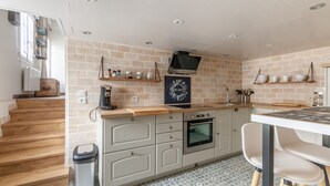 Une cuisine moderne avec un mur de briques en guise de crédence, des meubles en bois, un four encastré et un coin repas avec une table et des chaises.