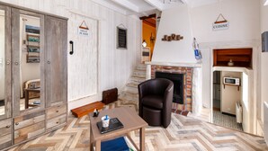 Une pièce chaleureuse avec un parquet en chevrons, une cheminée, un fauteuil en cuir et une table sur laquelle se trouvent un livre et une tasse.