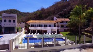 Un grand bâtiment doté d’une piscine, entouré d’une clôture, avec des palmiers en arrière-plan.