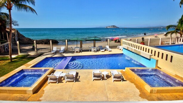 Un espace piscine doté de plusieurs bains à remous et de chaises longues, avec vue sur la plage et un ciel dégagé.