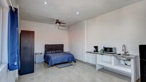 Une chambre à coucher comprenant un lit, une table de chevet, un bureau, une chaise, un ventilateur de plafond et une fenêtre avec des rideaux.