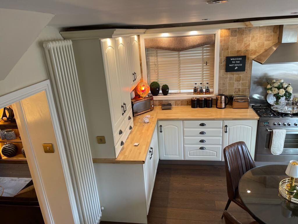 Una cocina con muebles blancos, encimera de madera, estufa y un comedor con mesa y sillas.