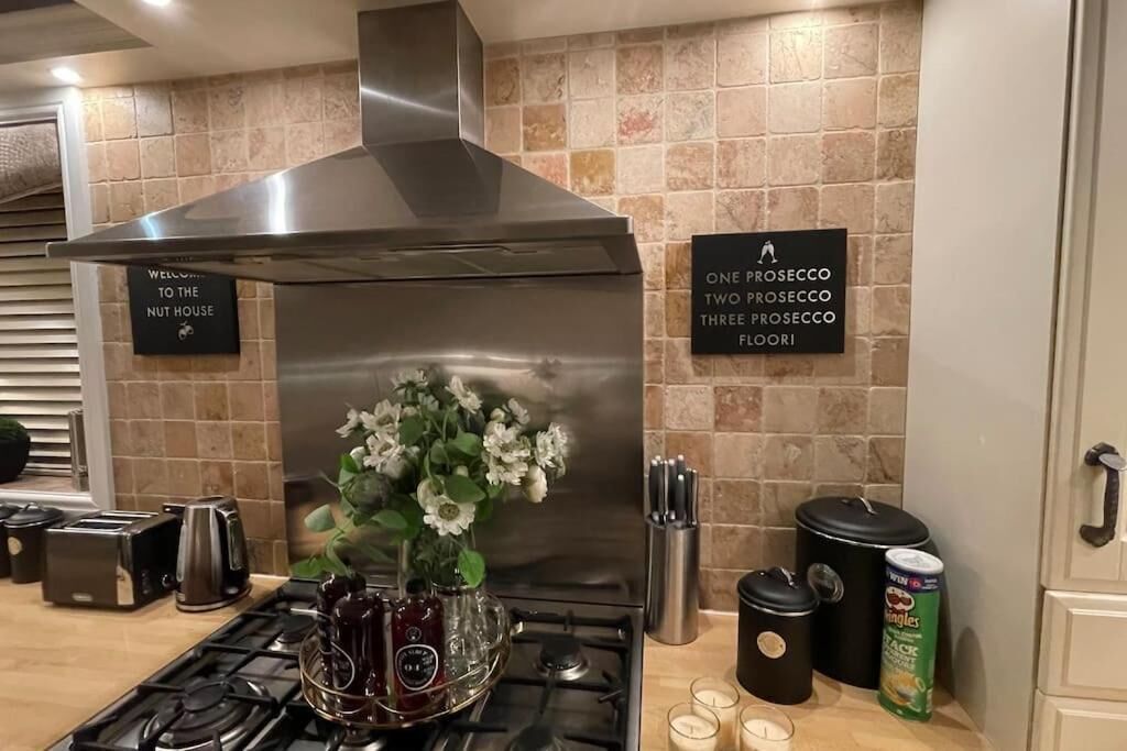 A kitchen with a stainless steel range hood, a flower vase, a toaster, a kettle, and a can of 'Chick-fil-A' on the counter.