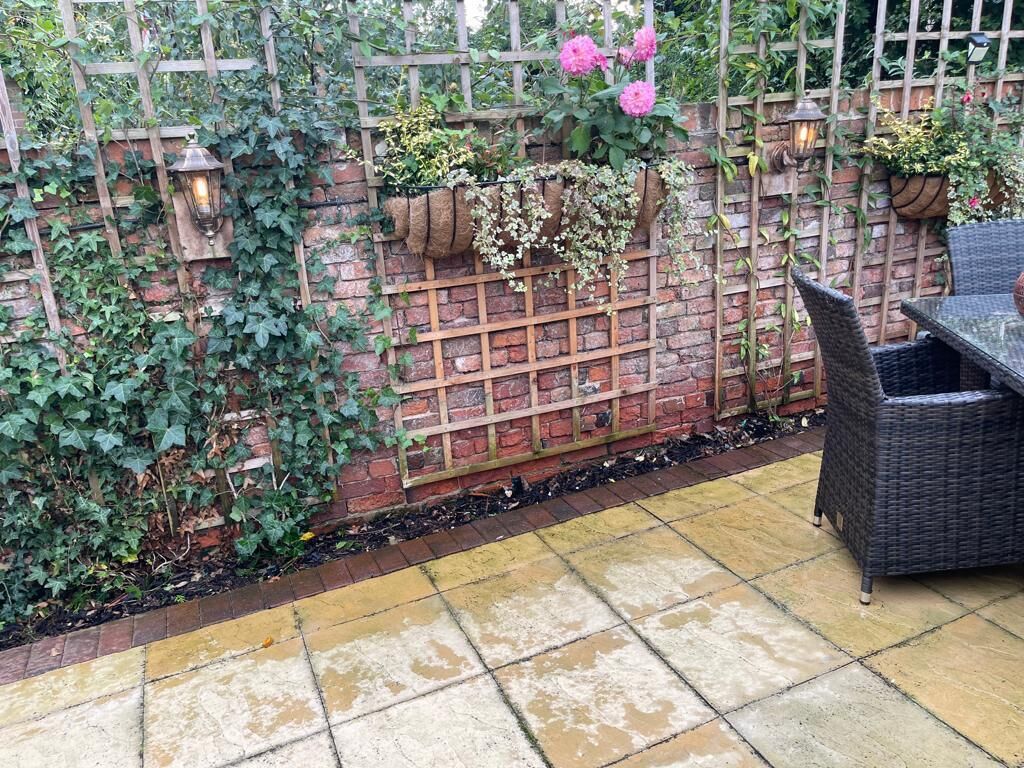 Un muro de ladrillo con celosía, macetas colgantes de flores y una silla de mimbre.