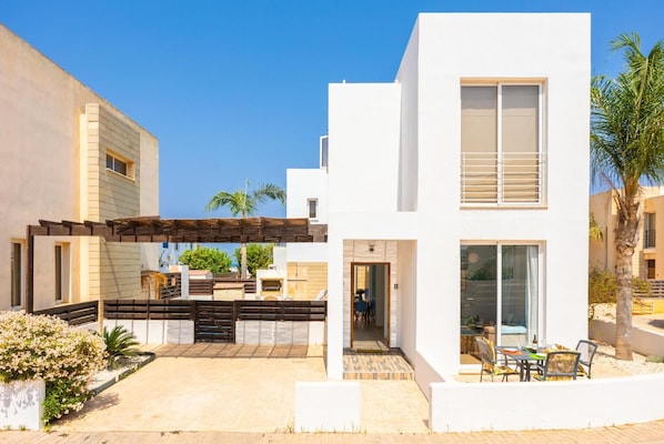 Una casa moderna de dos pisos con un patio, mobiliario exterior y un espacio cubierto.