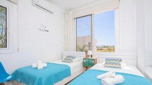 Hotellihuone, jossa on kaksi sänkyä, ikkuna, josta on näkymä, yöpöytä lampun kanssa ja seinäkoriste.