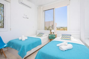 Habitación de hotel con dos camas, una ventana con vistas, una mesita de noche con lámpara y un adorno en la pared.