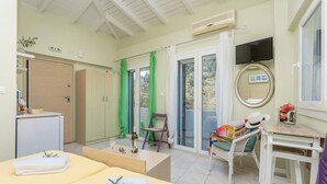 Una habitación con una cama, una silla, una mesa, un televisor y una puerta corrediza de vidrio al exterior.