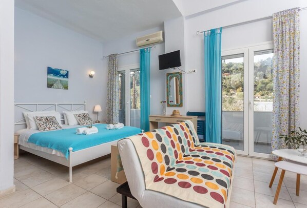 Une chambre à coucher comprenant un lit, un bureau, une télévision et un balcon avec des rideaux.