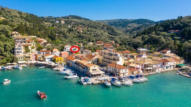 A coastal town with buildings along the waterfront, boats docked, and a hilly backdrop. - Niki Studio Tria - One Bedroom Apartment, Sleeps 2 (Lakka)