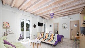 A spacious living area with a sofa, a small table, and a colorful sofa bed. There is a balcony with a view of the outdoors. - Niki Studio Tria - One Bedroom Apartment, Sleeps 2 (Lakka)