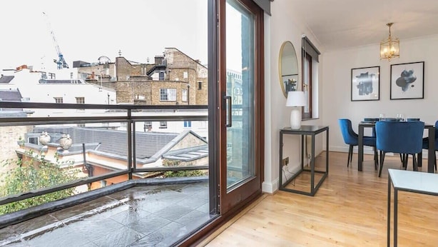 Un appartamento moderno con un ampio balcone, pavimento in legno, zona pranzo con sedie blu e vista sulla città.