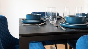 Zona pranzo con tavolo apparecchiato per quattro, sedie blu e due dipinti astratti alle pareti.