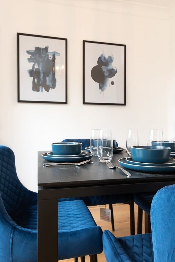 A dining area with a table set for four, blue chairs, and two abstract paintings on the wall.