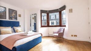 Una camera da letto con un letto grande, una finestra ad angolo, una sedia e opere d'arte alle pareti.