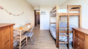 A compact room with bunk beds, a wooden desk, and a dining table. - 50 meters from the ski slopes, 9th floor, mountain view, pool, TV, ski locker, 16 m² (Le Corbier)