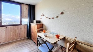 A small dining area with a wooden table and chairs, a cabinet, and a view through a window. - 50 meters from the ski slopes, 9th floor, mountain view, pool, TV, ski locker, 16 m² (Le Corbier)