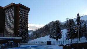 A swimming pool with a view of a tall building and a snowy mountain in the background. - 50 meters from the ski slopes, 9th floor, mountain view, pool, TV, ski locker, 16 m² (Le Corbier)