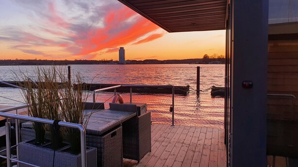 Terraza de madera con mobiliario exterior con vista a un cuerpo de agua al atardecer.