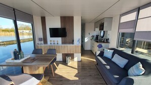 Un interior moderno con comedor, sofá, cocina y ventanas amplias con vista al agua.