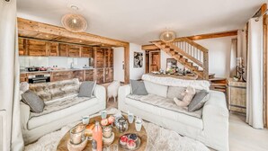 A cozy living room with two white sofas, a wooden coffee table with snacks, and a staircase leading to a dining area. - 50m from ski slopes, 5th floor, swimming pool, sauna, hammam, balcony, tv, ski locker, 93m², Tignes (Tignes)