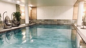 A large indoor swimming pool with clear blue water, surrounded by stone tiles and modern seating areas. - 50m from ski slopes, 5th floor, swimming pool, sauna, hammam, balcony, tv, ski locker, 93m², Tignes (Tignes)